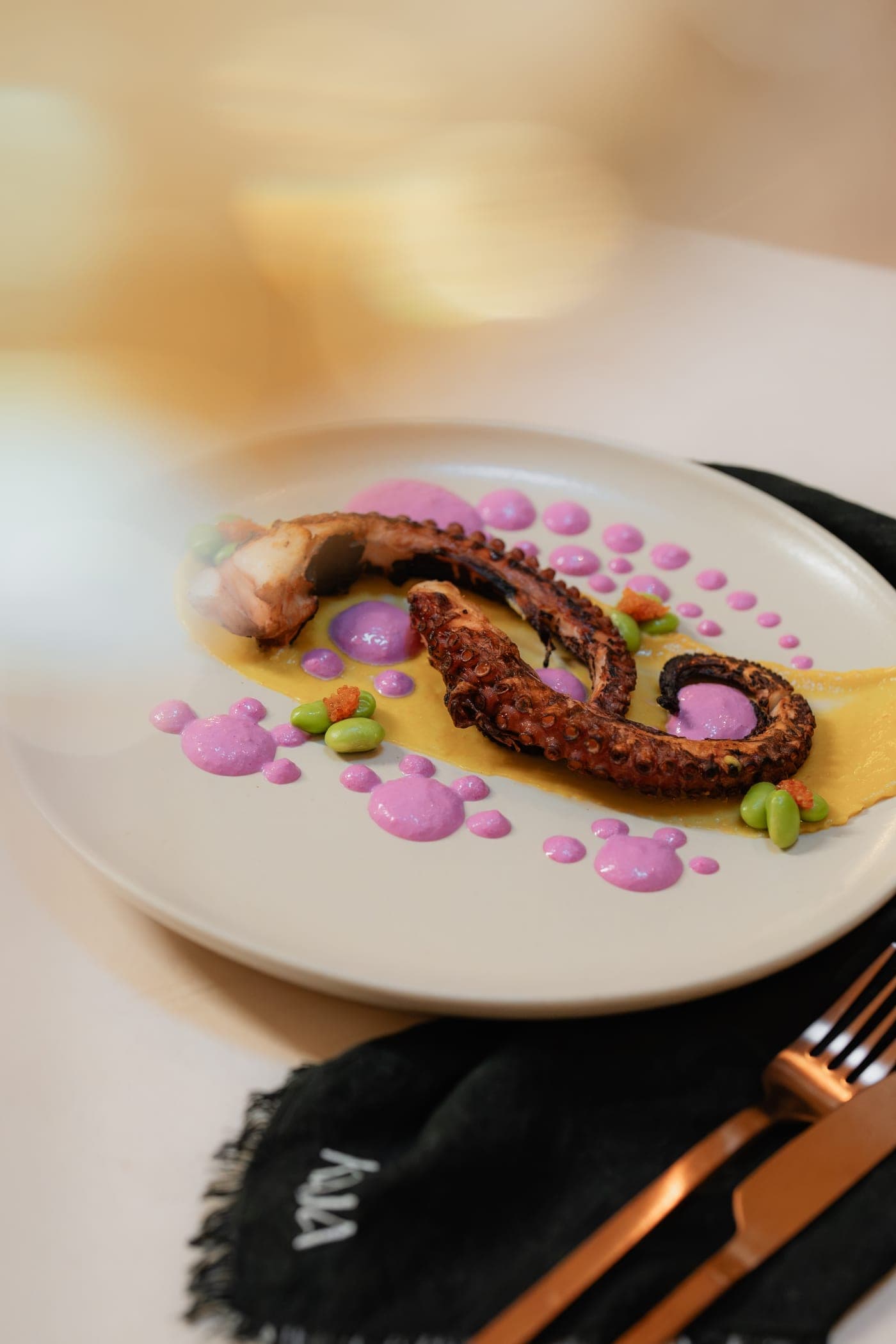 Grilled octopus with dots of pink purée, beside a KAJA-embossed napkin